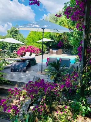 a patio with purple flowers and an umbrella and a pool at la VILLA GUIDI in Pila-Canale