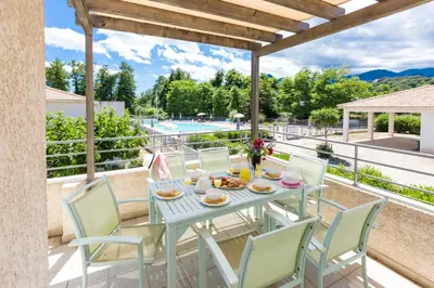 a table and chairs on a patio with a view of a pool at Résidence Odalys Acqua Bella in Poggio-Mezzana