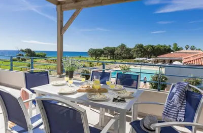 a table on the balcony with a view of the ocean at Résidence Odalys Acqua Bella in Poggio-Mezzana