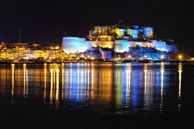 a large building with lights on the water at night at Villa entre Mer et Montagne... in Calenzana