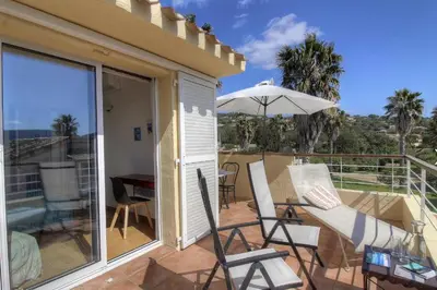 a patio with chairs and an umbrella on a balcony at Appartement 2 pièces Pied dans l'eau in Porto-Vecchio