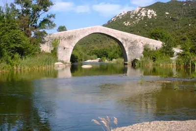 a stone bridge over a river with a mountain at Demeure traditionnelle en pierre avec piscine in Sartène