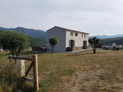 a white house with a car parked in a field at En plein maquis,entre mer&montagne in Vallecalle