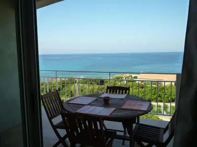 a table and chairs on a balcony with the ocean at APPARTEMENT PIED DANS L EAU ET VUE MER MAGNIFIQUE in Sartène