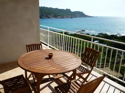 a wooden table and chairs on a balcony with the ocean at APPARTEMENT PIED DANS L EAU ET VUE MER MAGNIFIQUE in Sartène