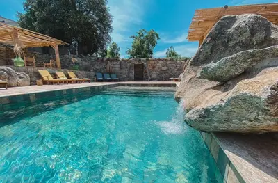 a swimming pool with a large rock next to a resort at Résidence de Luxe 4 étoiles à Pietralba, 4 logements piscine chauffée BALAGNE in Pietralba