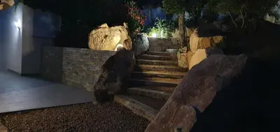 a set of stairs with a stone wall at night at Très belle Résidence vue mer et piscine chauffée - BACCALOCATION in Porto-Vecchio