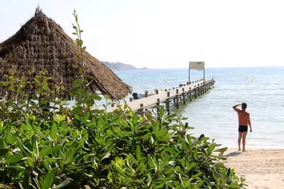 a man standing on a beach next to a pier at Hôtel & Lodges Moby Dick in Porto-Vecchio