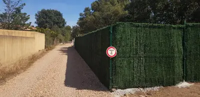 a green fence with a sign on it next to a road at Mini-villa 1 MER in Porto-Vecchio