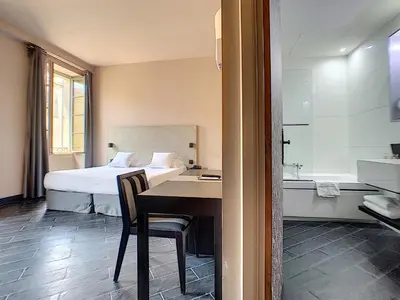 a bedroom with a bed and a desk and a bathroom at Hotel POZZO DI BORGO in Ajaccio