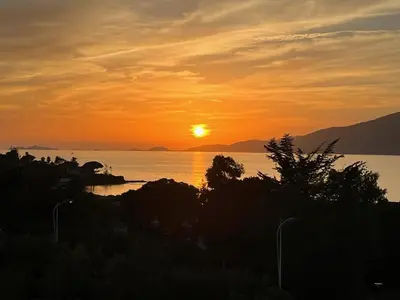 a sunset over a body of water with the sun setting at duplex vue mer exceptionnelle in Porticcio
