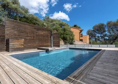 a swimming pool with a wooden deck next to a house at Le Haut de la Vague in Porto-Vecchio