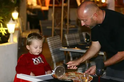 a young boy sitting next to a man cutting a pizza at Residence U Veniqui in Favone