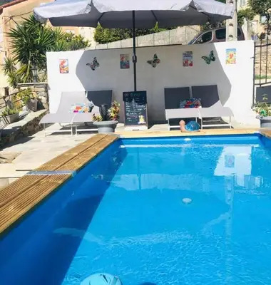 a swimming pool with an umbrella and blue water at Gîte Emma in Santo-Pietro-di-Tenda