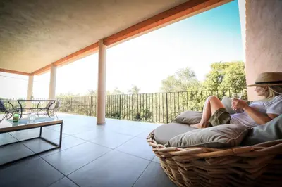 a woman sitting on a wicker couch on a porch at SARL Valinco locations appartement 2 chambres in Olmeto