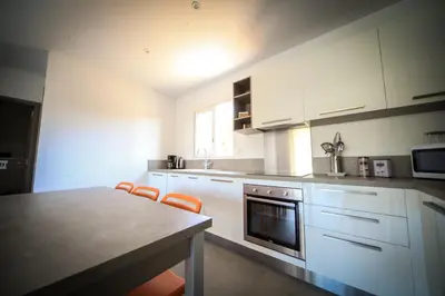 a kitchen with white cabinets and a table with orange chairs at SARL Valinco locations appartement 2 chambres in Olmeto