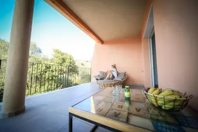 a woman sitting in a chair on a balcony with a table at SARL Valinco locations appartement 2 chambres in Olmeto