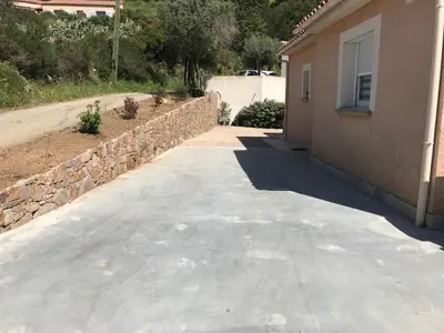 an empty driveway next to a house with a stone wall at ELI&LOU avec piscine in Alata