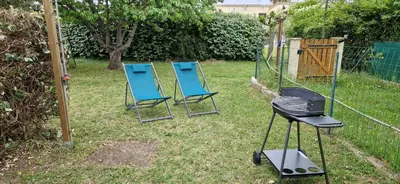 two blue chairs and a grill in a yard at Mini villa au bord de la mer, proche Moriani (Corse) in Poggio-Mezzana