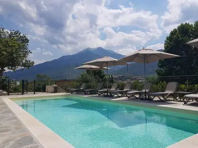 a pool with chairs and umbrellas with mountains in the background at Si Mea in Corte