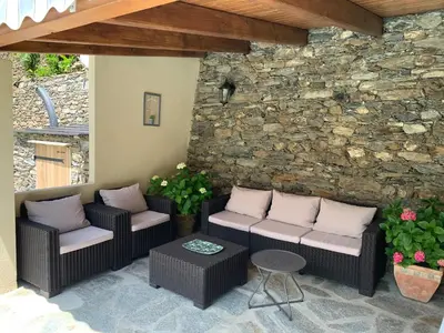 a patio with two wicker chairs and a stone wall at LA SOURCE 4 chambres in Valle d'Alesani