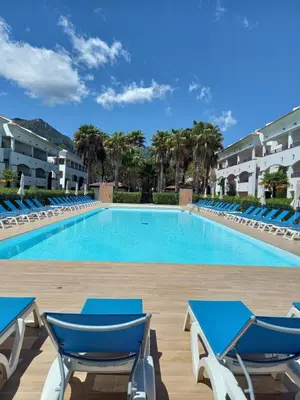 a large swimming pool with blue chairs and palm trees at Appartement avec piscine vue mer et montagne in San-Nicolao