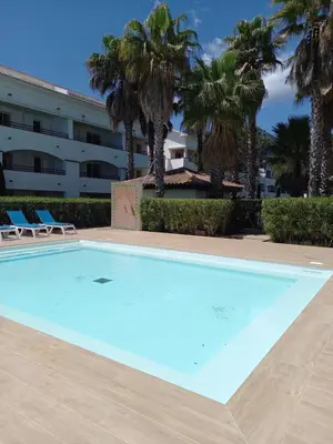 a swimming pool with palm trees and a building at Appartement avec piscine vue mer et montagne in San-Nicolao