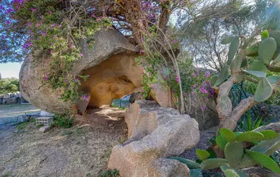 a cave in a rock with a tree and flowers at Pet Friendly Apartment in Pianottoli-Caldarello