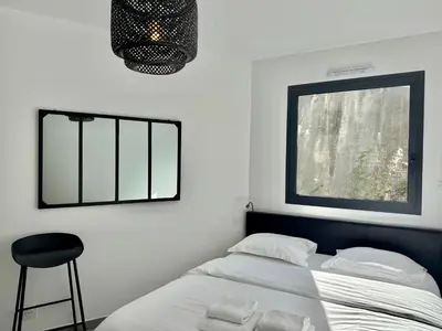 a bedroom with a bed and a window and a stool at Appartement neuf tout confort en bord de mer in Propriano