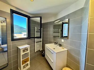 a bathroom with a sink and a toilet and two windows at Appartement neuf tout confort en bord de mer in Propriano