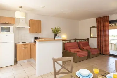 a kitchen and living room with a table and chairs at Résidence Odalys Les Hameaux de Capra Scorsa in Belgodère
