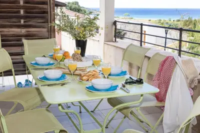 a table with breakfast food on a balcony with the ocean at Résidence Odalys Les Hameaux de Capra Scorsa in Belgodère