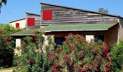 an old house with red windows and some bushes at Résidence Marina di Capitello in Porticcio
