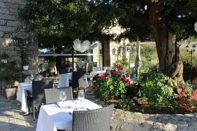 a restaurant with white tables and chairs under a tree at Hôtel & Résidence Les Bergeries d'Alata in Alata