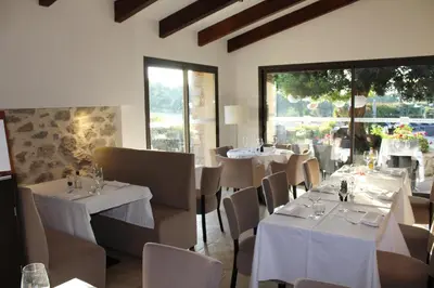 a dining room with white tables and chairs and windows at Hôtel & Résidence Les Bergeries d'Alata in Alata