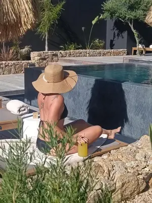 a woman in a hat sitting next to a swimming pool at Hôtel Les Suites Du Maquis in Bonifacio