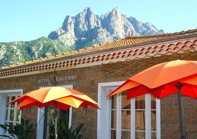 two umbrellas in front of a building with mountains in the background at Hôtel Colombo- Porto Corse in Porto Ota