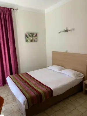 a bedroom with a bed with a pink curtain at Hôtel Colombo- Porto Corse in Porto Ota