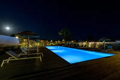 a swimming pool at night with chairs and an umbrella at Calarossa Bay Resort in Porto-Vecchio