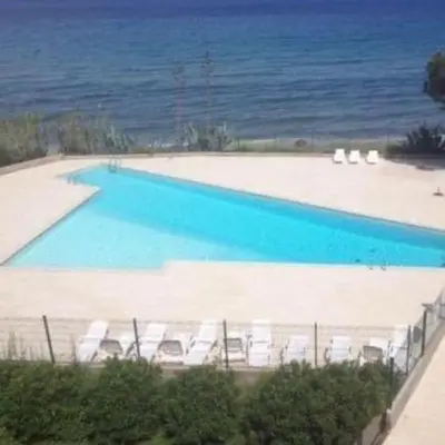 a large swimming pool with white chairs and the ocean at Residence Santa Lucia, studio avec piscine , vue mer et pied dans l'eau , Moriani-Plage in Santa-Lucia-di-Moriani