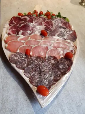 a heart shaped pizza with meat and tomatoes on a table at Alegria in Arbellara
