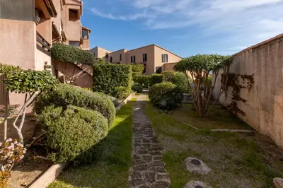 a garden with bushes and a walkway between two buildings at La Punta Geronimi in Porto Pollo