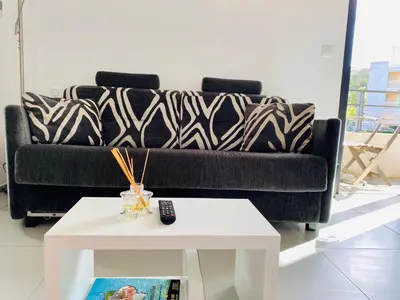 a living room with a black couch and a white table at Studio tout confort en centre ville in Propriano