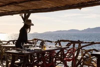 a woman sitting at a table in front of the water at Villa Kirssis in Porticcio