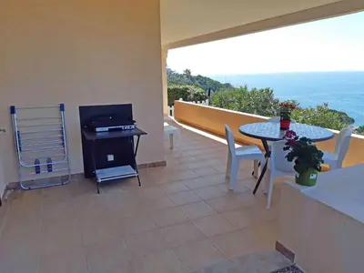 a patio with a table and a television on a balcony at Soleil Topaze - 68 m2 - Terrasse - Jardinet - Transats - Vue mer panoramique sur toute la baie in Porticcio