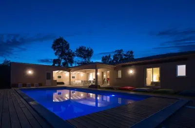a large swimming pool in front of a house at night at Villa Poggio Rosso - Pool-House & Piscine chauffée in Sainte-Lucie de Porto-Vecchio