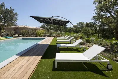a row of lounge chairs and an umbrella next to a pool at Villa Poggio Rosso - Pool-House & Piscine chauffée in Sainte-Lucie de Porto-Vecchio
