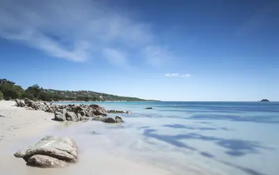 a beach with rocks and the ocean on a sunny day at Villa Poggio Rosso - Pool-House & Piscine chauffée in Sainte-Lucie de Porto-Vecchio