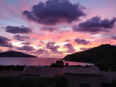 a sunset over the water with houses and a mountain at Demi villa à 150m de la plage avec vue sur mer in Appietto