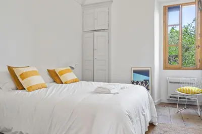 a white bedroom with a large bed and a window at Cargèse, appartement de charme surplombant le port in Cargèse